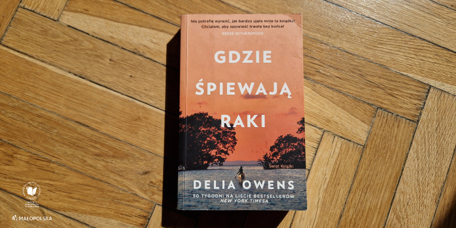 Na oświetlonej słońcem drewnianej podłodze żółta okładka książki "Gdzie śpiewają raki" Delii Owens